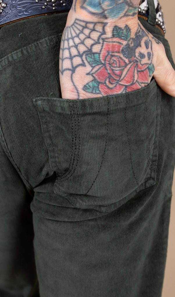 Close up of the stitching detail on the pocket of the forest green corduroy bell bottom flares with James' tattooed hand resting in the pocket.