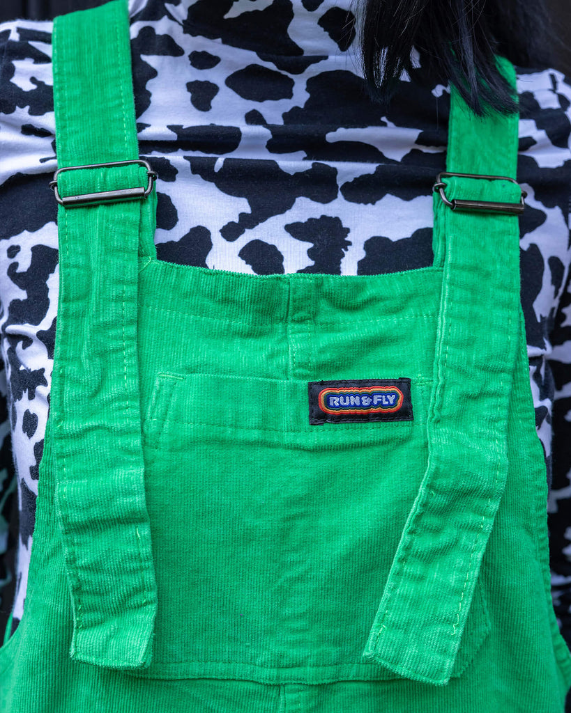 Gabriella a tall black haired model is wearing a green pair of corduroy dungarees with a cow print polo neck on underneath. She is against a black garage door in a mews shot by Amy Davies Photography in Hove