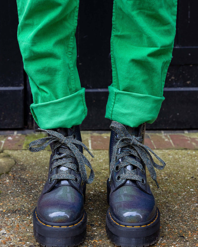Gabriella a tall black haired model is wearing a green pair of corduroy dungarees with a cow print polo neck on underneath. She is against a black garage door in a mews shot by Amy Davies Photography in Hove.