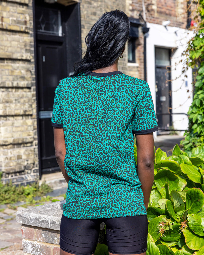 Yolande is wearing Teal Leopard Print T Shirt with black trousers. She is stood outside in Hove on a sunny day smiling at the camera and holding onto the bottom of the t shirt.