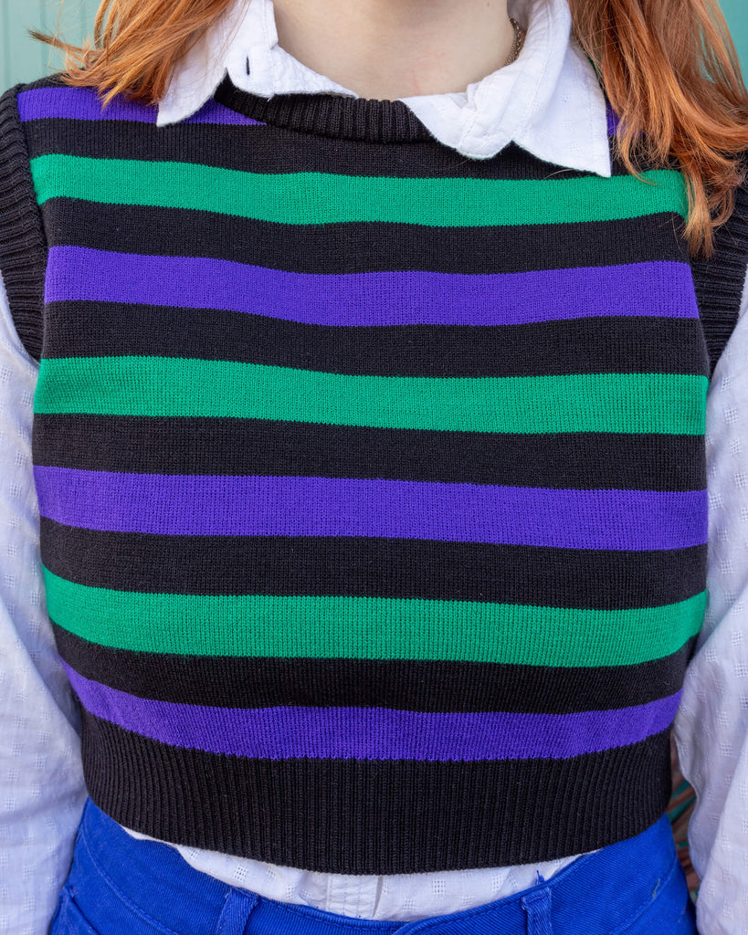 Tasha a tall red haired femme model is wearing a white shirt and green, black and purple striped tank from Run & Fly with blue jeans against a mews background