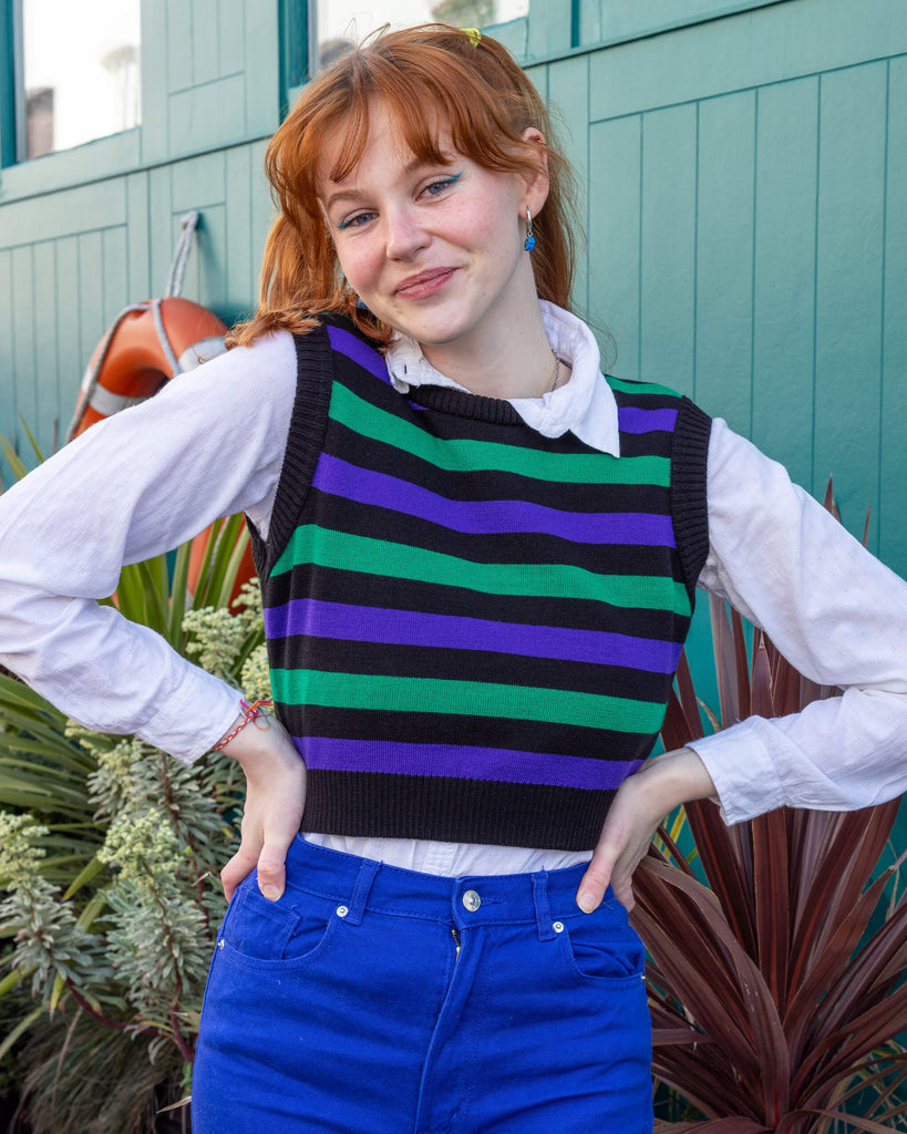 Tasha a tall red haired femme model is wearing a white shirt and green, black and purple striped tank from Run & Fly with blue jeans against a mews background