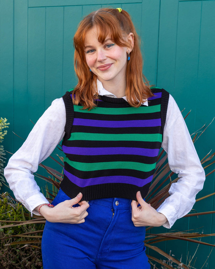 Tasha a tall red haired femme model is wearing a white shirt and green, black and purple striped tank from Run & Fly with blue jeans against a mews background