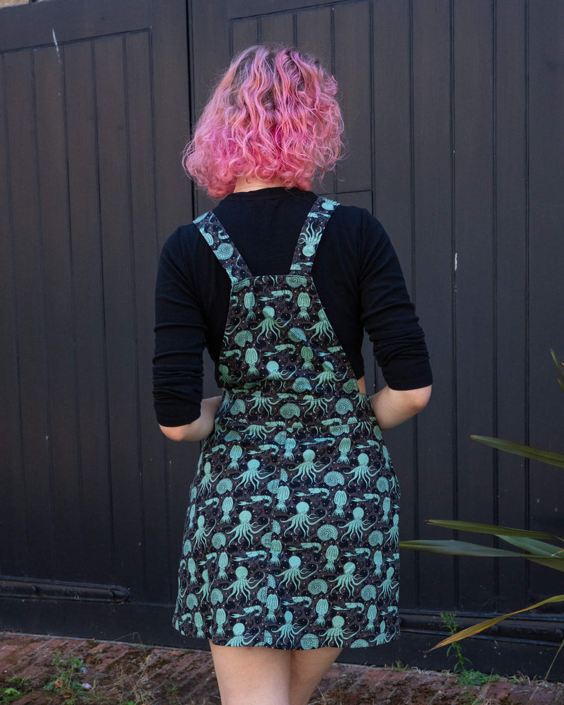 Back view of the Run & Fly green sea creatures pinafore dress, showing the straps and flow of the marine print. The dress features an octopus, squid, and nautilus print.