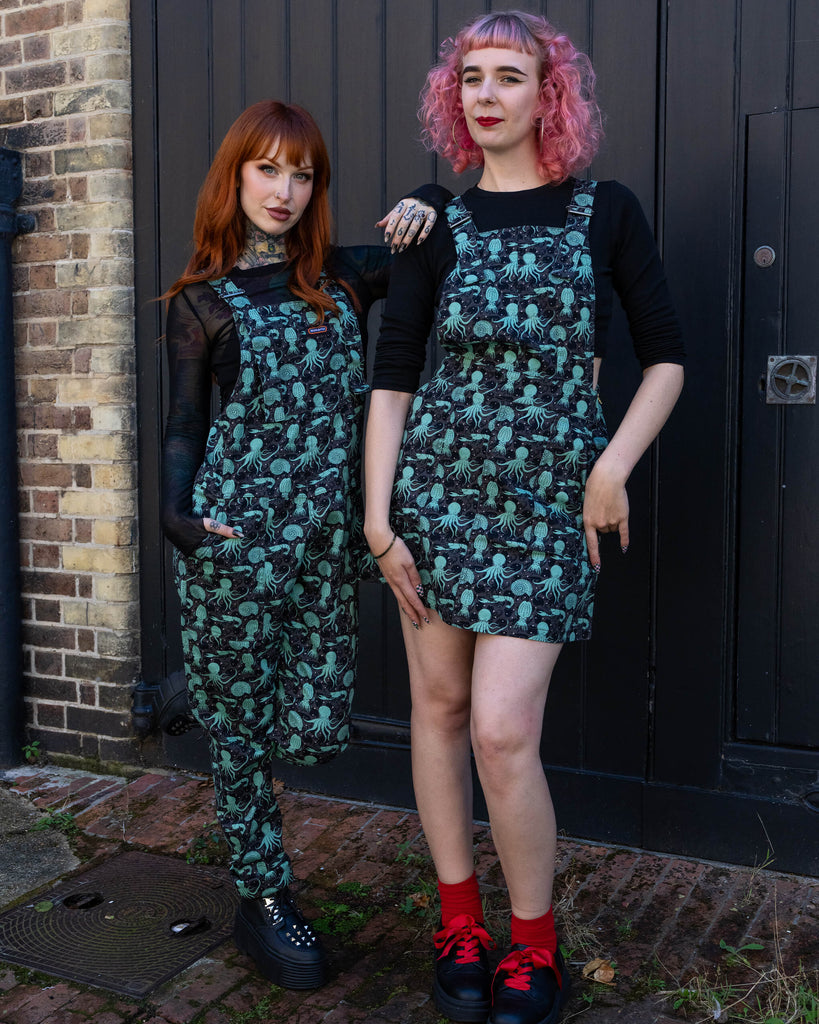 Two women posing together, both wearing the Run & Fly green sea creatures print. One wears dungarees, and the other a pinafore dress, both showcasing the same whimsical marine design.