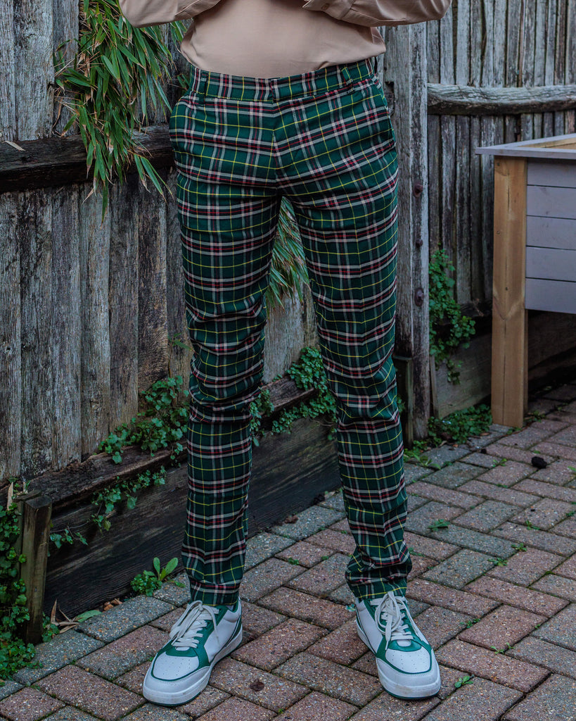 Close-up of the full length of Run & Fly Retro Mod Stretch Plaid Green Tartan Slim Skinny Fitting Trousers, paired with green and white trainers. Jack models the trousers with a beige long-sleeved top. Run & Fly creates sustainable, ethical clothing with a retro twist.