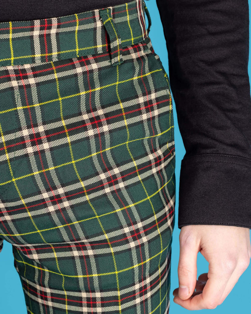  Close up shot of the front side pocket on the retro mod stretch plain green tartan slim skinny fitting trousers, , worn with a long sleeve black shirt in front of a blue studio background.