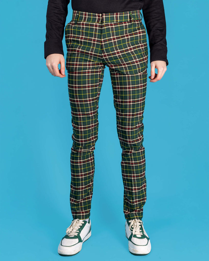 Jack is stood in front of a blue studio background wearing the retro mod stretch plaid green tartan slim skinny fitting trousers with a long sleeve black shirt and white trainers. They are facing forward with both arms resting by their side. Photo is cropped from the waist down.