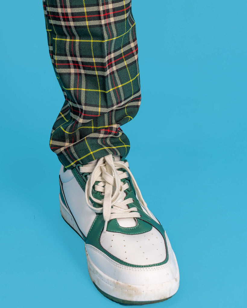 Close up shot of Jack's ankle wearing the retro mod stretch plaid green tartan slim skinny fitting trousers, worn with white trainers in front of a blue studio background.