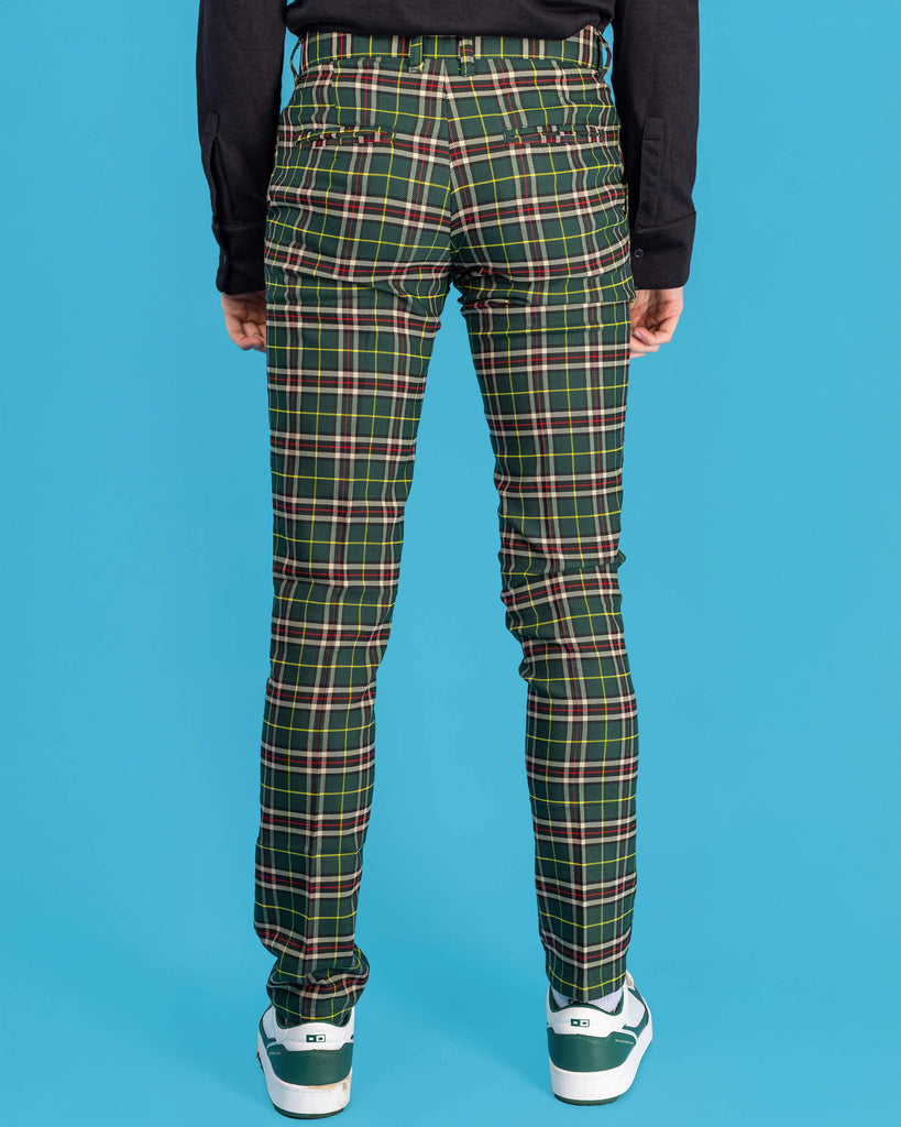Jack is stood in front of a blue studio background wearing the retro mod stretch plaid green tartan slim skinny fitting trousers with a long sleeve black shirt and white trainers. They are facing away from the camera with both arms resting by their side. Photo is cropped from the waist down.