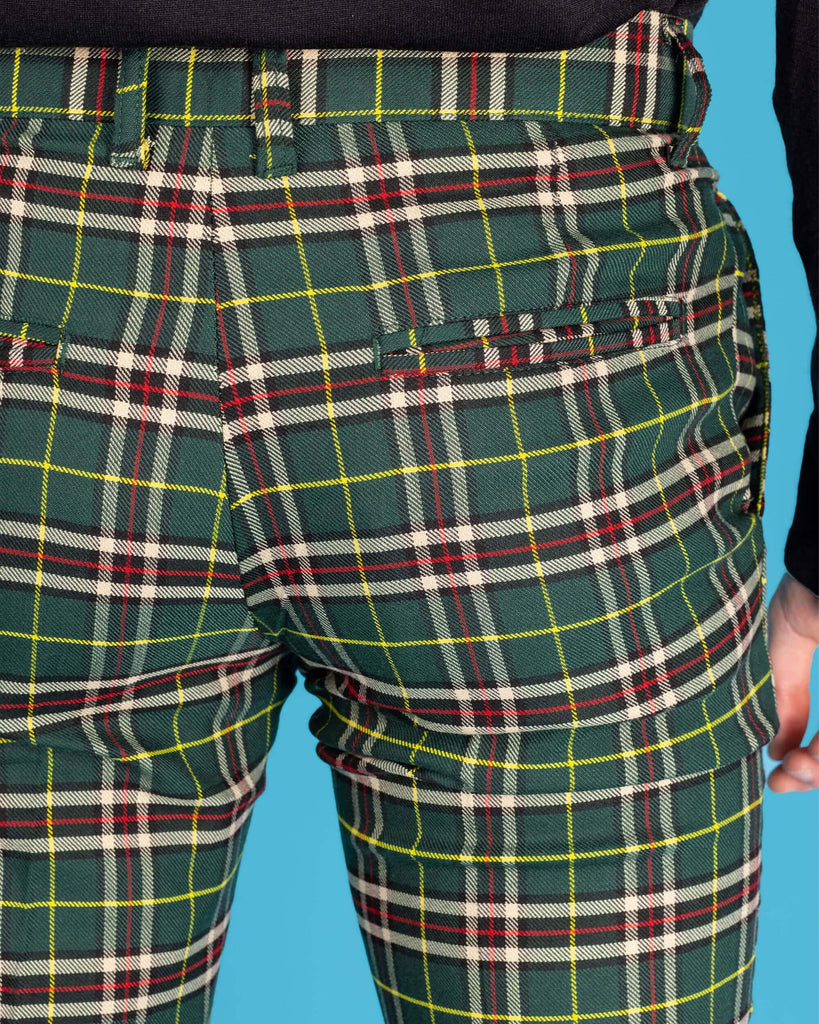 Close up shot of the back pocket on the retro mod stretch plaid green tartan slim skinny fitting trousers, worn with a long sleeve black shirt in front of a blue studio background.