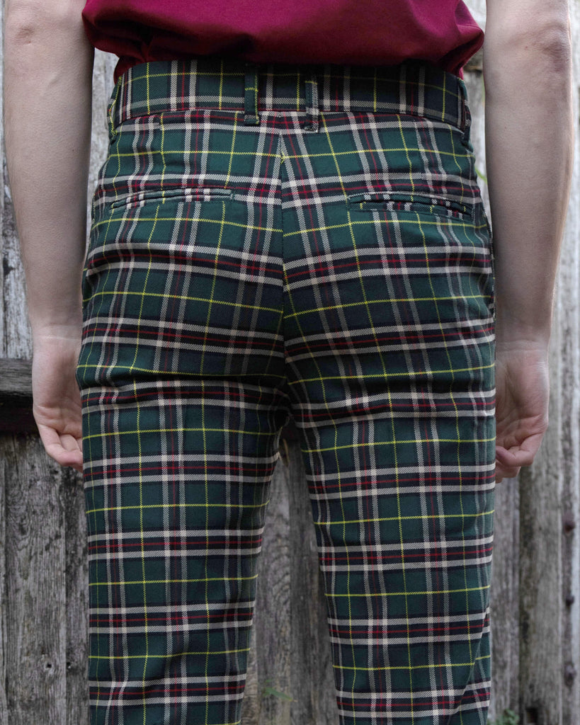 close up of Jack stood in front of a fence wearing the green tartan plaid bell bottom slacks. He is facing away from the camera with both hands resting by his sides. Photo is cropped from the waist down.