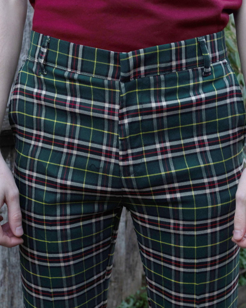 close up of Jack stood in front of a fence wearing the green tartan plaid bell bottom slacks. He is facing toward the camera with both hands resting by his sides. Photo is cropped from the waist down.