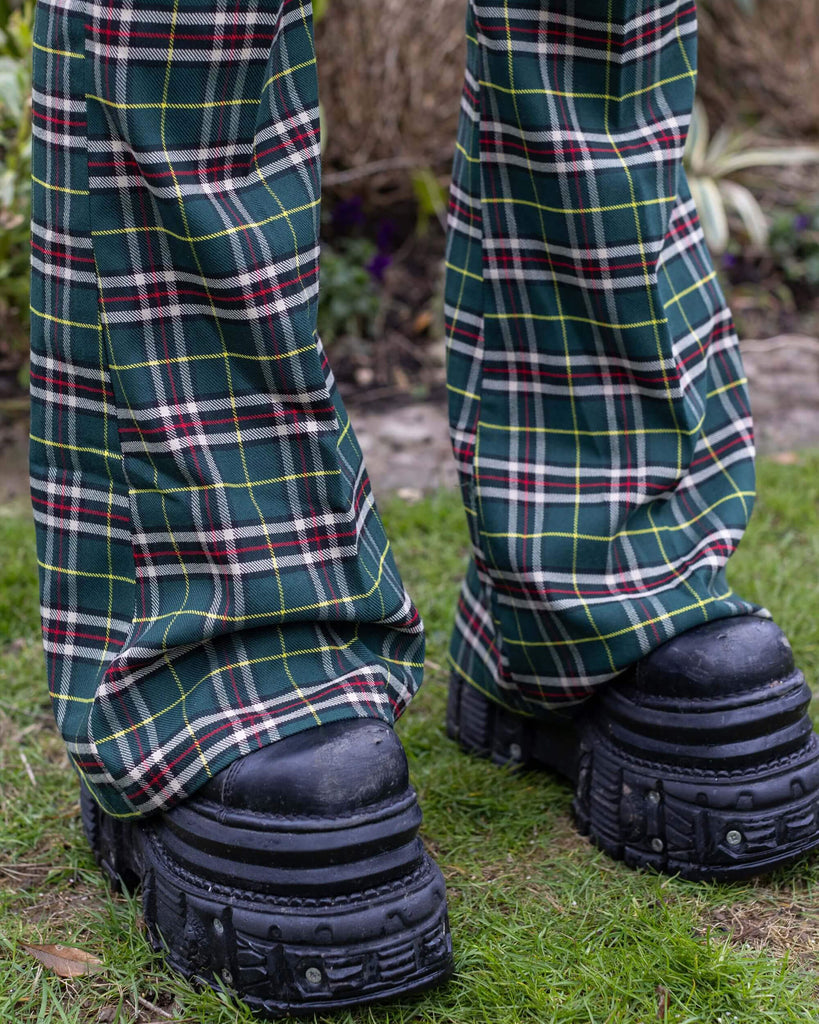 Close up of Florence wearing Green Tartan Plaid Bell Bottom Slacks.  Close up shows chunky black boots poking out from under the flared bottoms of the trousers. 