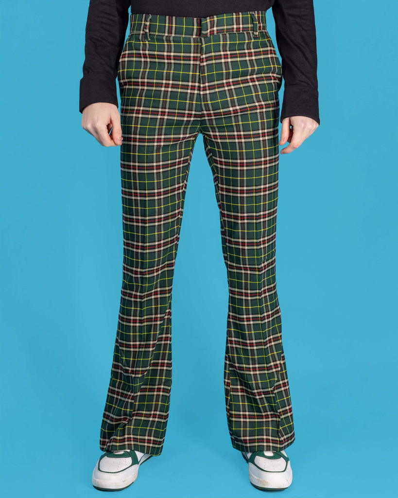 Jack is stood in front of a blue studio background wearing the green tartan plaid bell bottom slacks with a long sleeve black tshirt and white trainers. He is facing the camera with both hands resting by his sides. Photo has been cropped from the waist down.