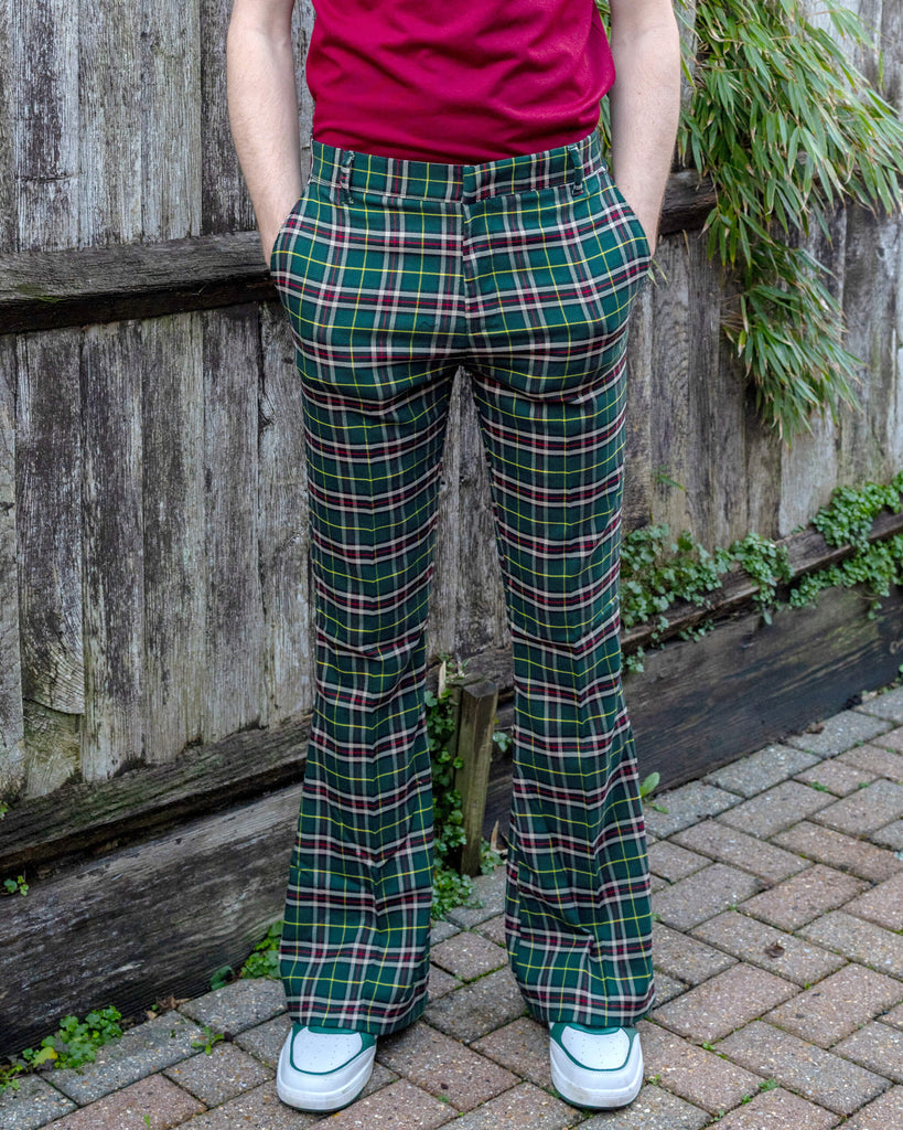 Jack is stood outside in a garden area wearing the green tartan plaid bell bottom slacks with white trainers. He is posing facing the camera with both hands in the front pockets. Photo is cropped at the waist