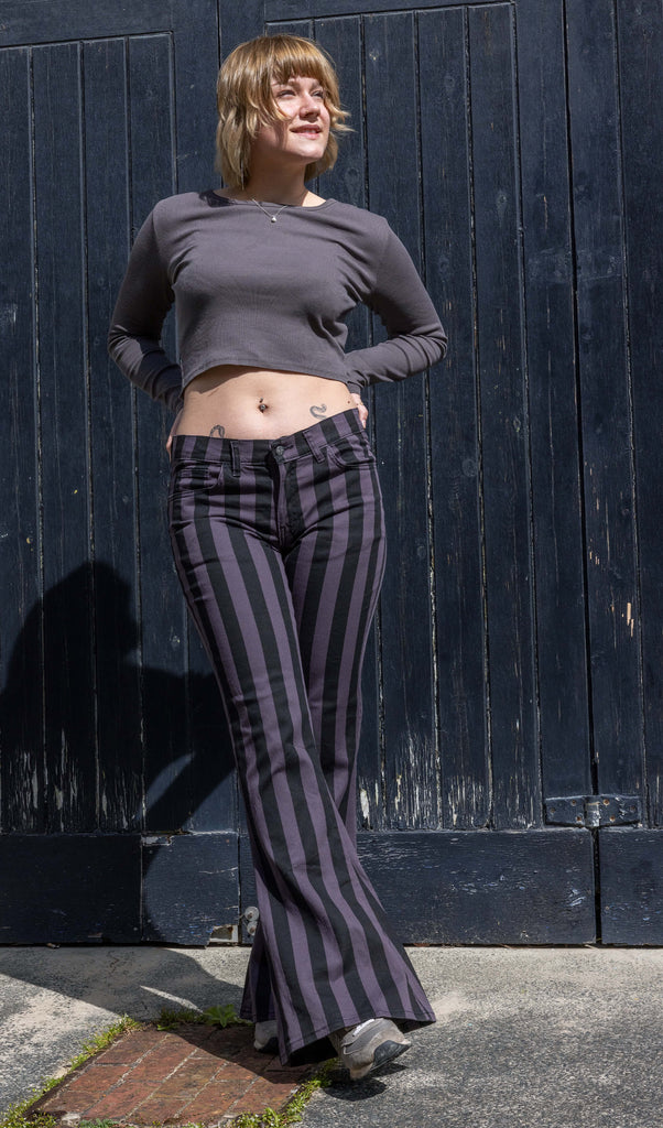 Julia is a female model in her 20's with short blonde hair. She is standing by a black garage door and wearing black and grey flares with a matching grey top 