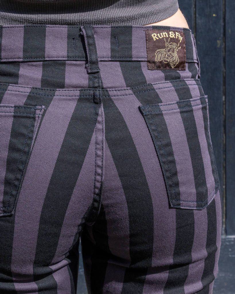 Close-up of the back pockets and waistband of Run & Fly grey and black vertical striped flare trousers. The trousers feature the brand's logo patch on the back, showcasing the small ethical slow fashion company's attention to detail. High-waisted and made with sturdy fabric, perfect for retro and alternative styles. Made in England.