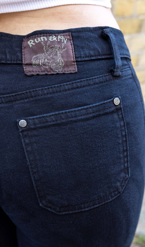 close up of Melia a white femme person wit dyed caramel coloured hair is smiling wearing a white vest and black hippy flares by Run & Fly stood in a mews in Hove