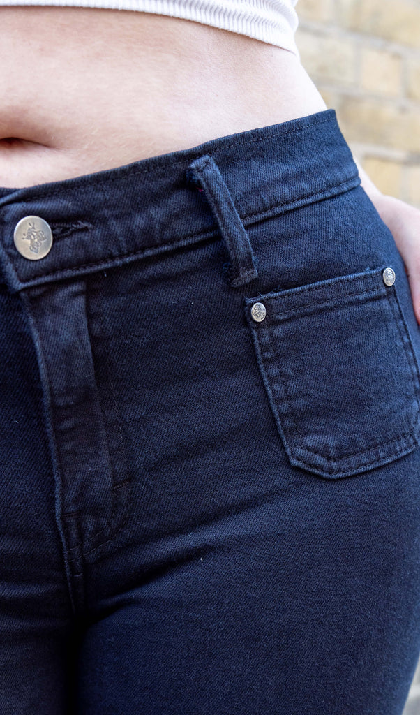 close up of Melia a white femme person wit dyed caramel coloured hair is smiling wearing a white vest and black hippy flares by Run & Fly stood in a mews in Hove