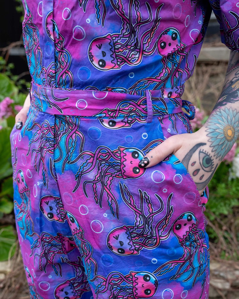 Side close-up of the waist and pocket area of the Run & Fly Jellyfish Stretch Jumpsuit, showing the matching fabric tie belt and fun underwater-themed jellyfish pattern.