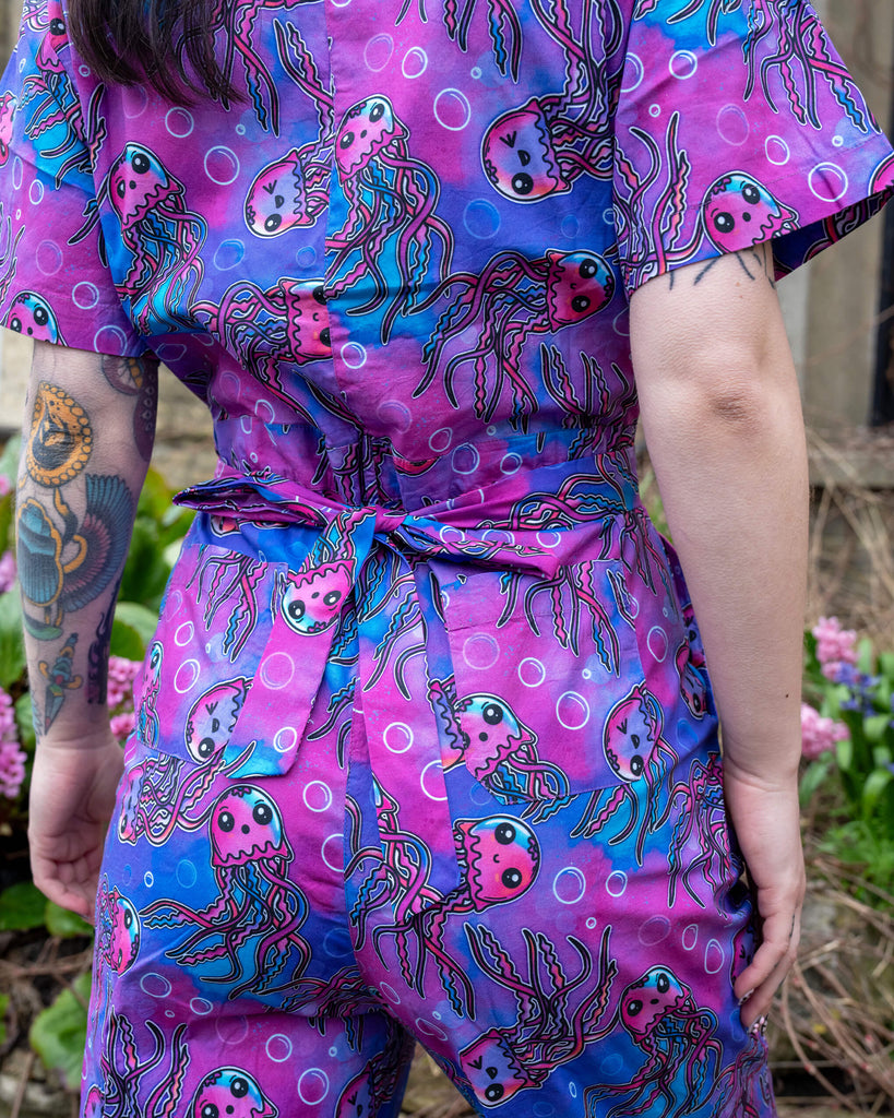 Rear close-up of the Run & Fly Jellyfish Stretch Jumpsuit showing the self-tie waist belt and detailed jellyfish print in shades of pink, purple, and blue.