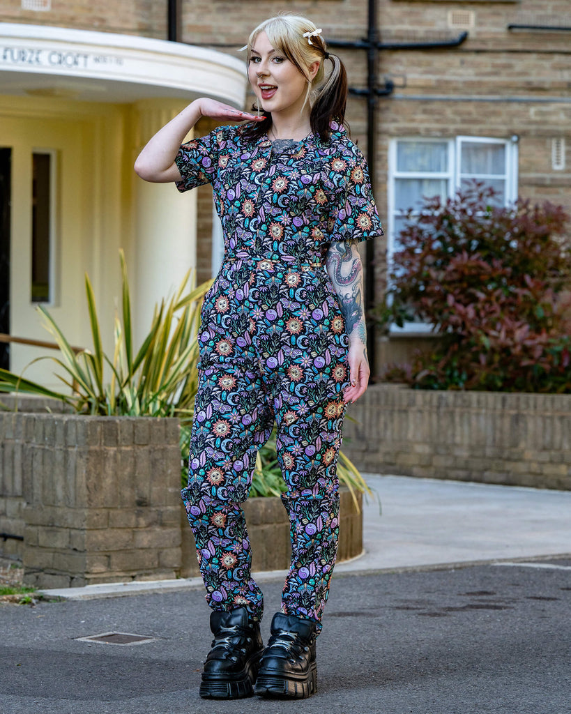 Model poses outdoors in the Boho Summer Stretch Jumpsuit by Run & Fly, featuring a colourful mystical print with suns, moons, crystals, and butterflies. Made ethically by a small slow fashion brand.