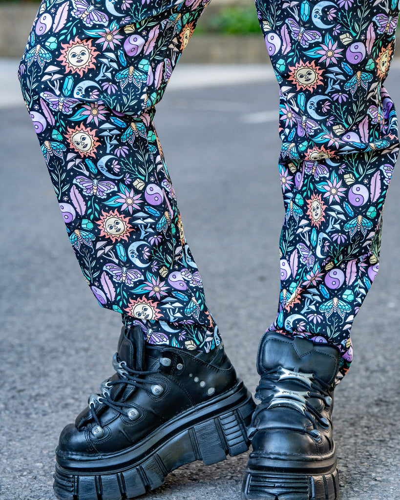 Close up of he Boho Summer Stretch Jumpsuit legs by Run & Fly styled with chunky black platform shoes. The all-over vibrant print includes sun faces, yin-yangs, and moths. Ethical, fun fashion.