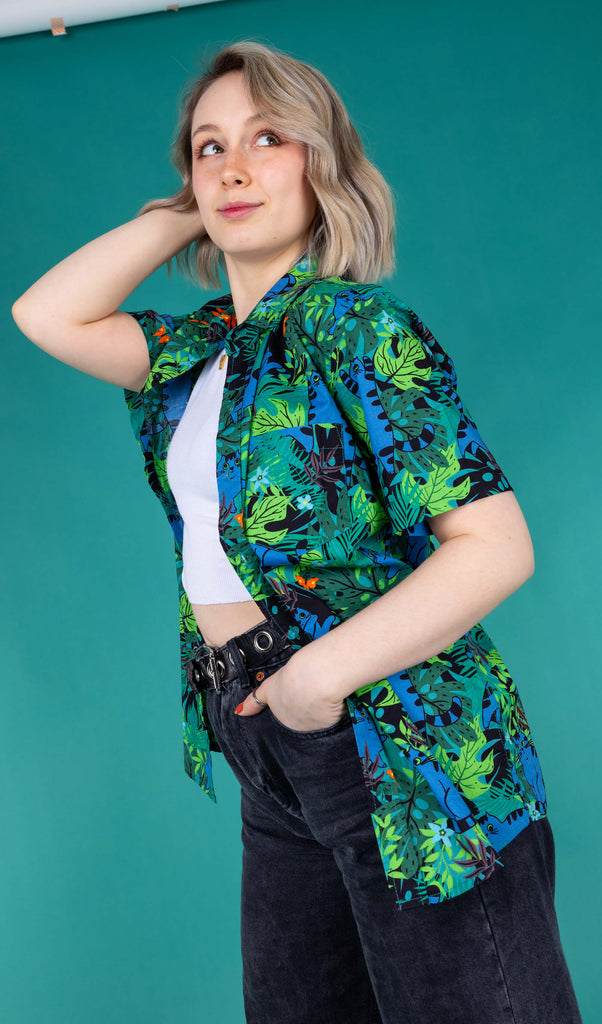 Amy  a blonde femme white model is wearing a Run & Fly shirt with cute fat blue cats in a jungle scene with a white vest and black jeans against a green background shot by Amy Davies Photography 