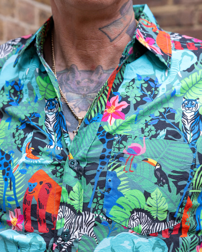 Close up shot of James wearing Jungle Stretch Short Sleeve Shirt. The collared shirt is a forest green colour with all over print of various jungle animals and plants in black, white, red, pink, yellow and blue. Close up shows shirt collar and print.