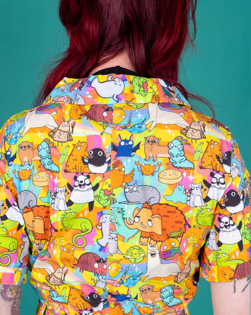 Florence a red haired female model with tattoos and cool make up is wearing a colourful rainbow jumpsuit with cute drawing by Katie Abey. She is standing against a turquoise background this is a close up of the top of the back of the garment