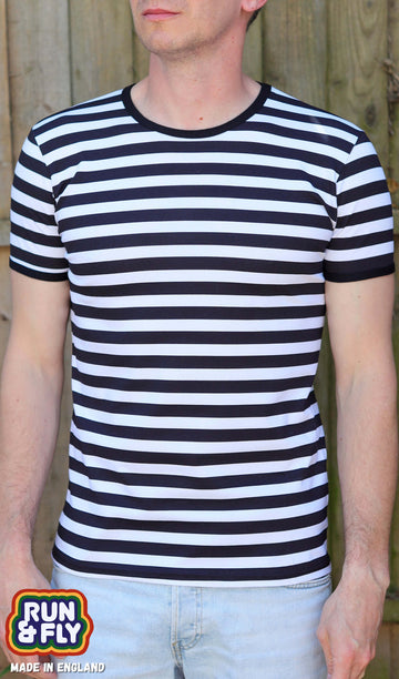 Model standing in front of a wood fence, is facing the camera wearing a black and white horizontally striped short sleeve t-shirt with light wash denim jeans. Photo is cropped from the chin to hips.