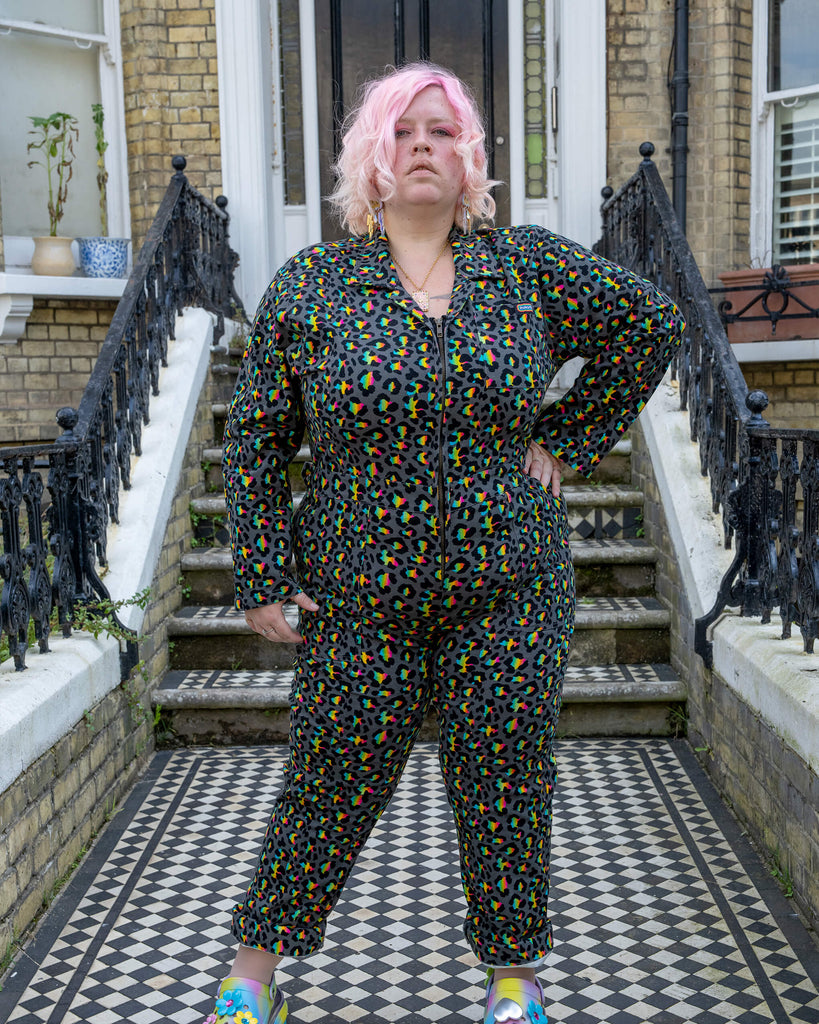 A confident model with pink hair poses in the Rainbow Leopard Stretch Twill Boiler Suit by Run & Fly. The multicoloured leopard print stands out in contrast to the monochrome tiled steps of a townhouse. The ethical slow fashion brand creates bold, creative pieces designed for self-expression.
