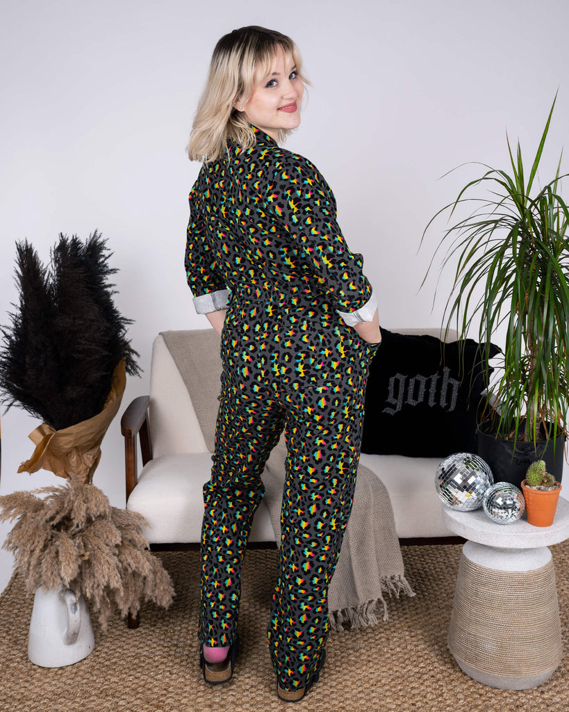 Back view of the Rainbow Leopard Stretch Twill Boiler Suit by Run & Fly, showing off its rainbow leopard print and elasticated waist for a flattering fit. The model strikes a fun, over-the-shoulder pose in a chic interior setting with gothic-inspired details.