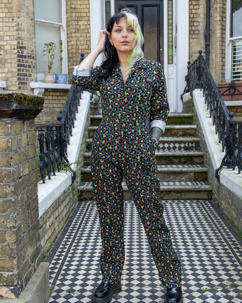 A second model with black and green split-dyed hair wears the Rainbow Leopard Stretch Twill Boiler Suit by Run & Fly while standing in front of a classic English townhome. The bold, colourful leopard print contrasts with the model’s edgy, street-style vibe. This ethical slow fashion piece offers an alternative, eye-catching outfit with a fun twist.