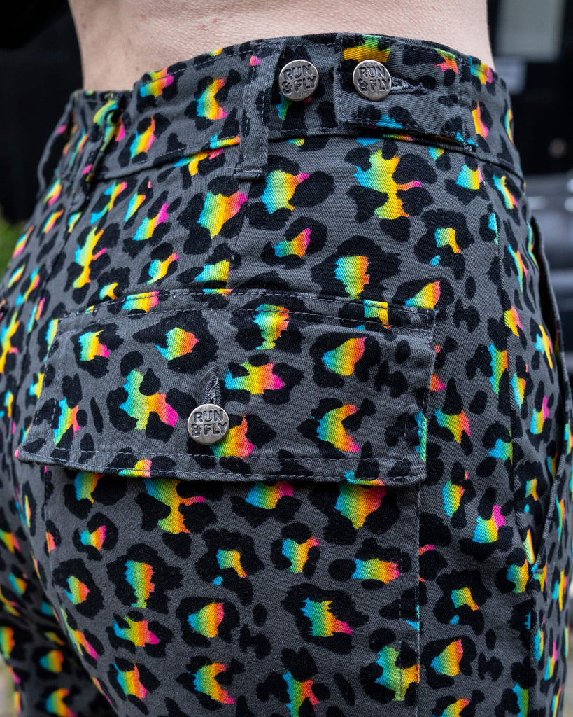 Close-up detail of the back pocket and waistband of the Run & Fly Grey Rainbow Leopard Straight Leg Trousers, showing the colourful rainbow leopard print on grey with silver Run & Fly button details.