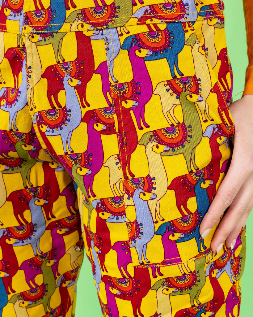 A close-up of the pocket area of the yellow llama print dungarees by Run & Fly. The vibrant pattern features bold, multicoloured llamas, creating a fun, playful aesthetic. The bright yellow background enhances the colourful design. Run & Fly is a small, ethical, slow fashion company.