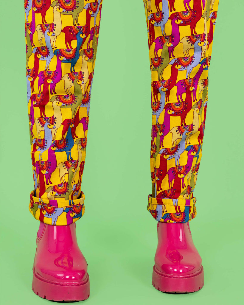 Close-up of the lower legs of the yellow llama print dungarees by Run & Fly. The playful, multicoloured llamas in reds, blues, and purples pop against the bright yellow fabric. The model pairs the dungarees with pink platform boots, adding extra fun to the quirky design. Run & Fly is a small, ethical, slow fashion company.