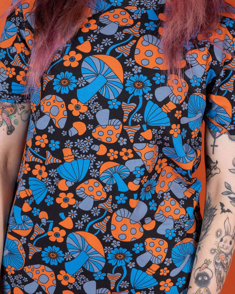 Close up of Sarah wearing the Magic Mushroom Short Sleeve Tee. She is facing forward to highlight the tshirt front. The magic mushroom print is a black base tshirt with blue and neon orange toadstool mushrooms and daisy shape flowers all over.
