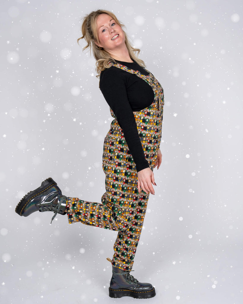 A playful full-length photo of Karina wearing Nutcracker print dungarees. She stands on one leg with the other kicked back, showing off her holographic platform boots. The snowy background adds to the festive vibe.