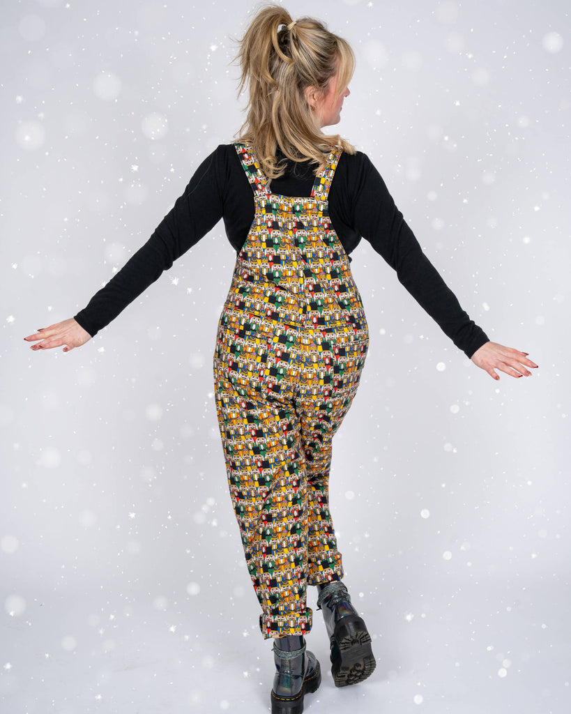 A back view of Karina modelling Nutcracker dungarees. She poses with her arms outstretched, highlighting the relaxed fit and vibrant pattern of the outfit.