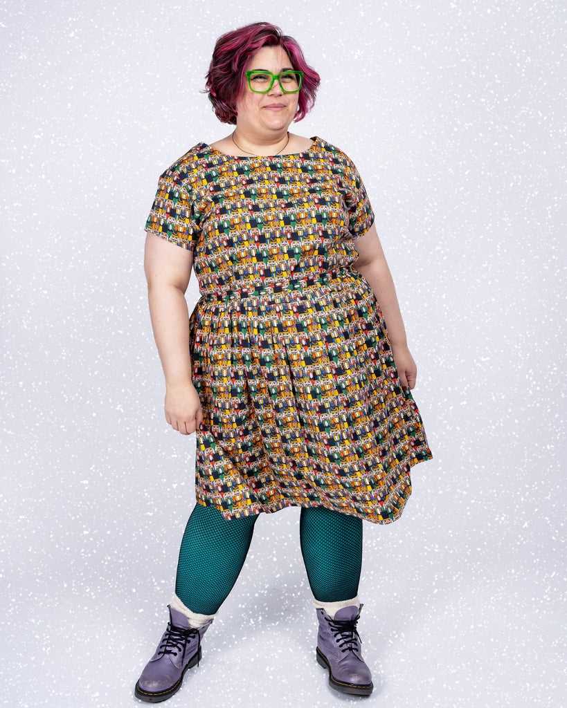 Jackie wears a Run & Fly tea dress featuring the Nutcracker print by Waffle Mama. The design includes colourful Nutcracker figures on a deep black background, paired with teal leggings and lilac boots.