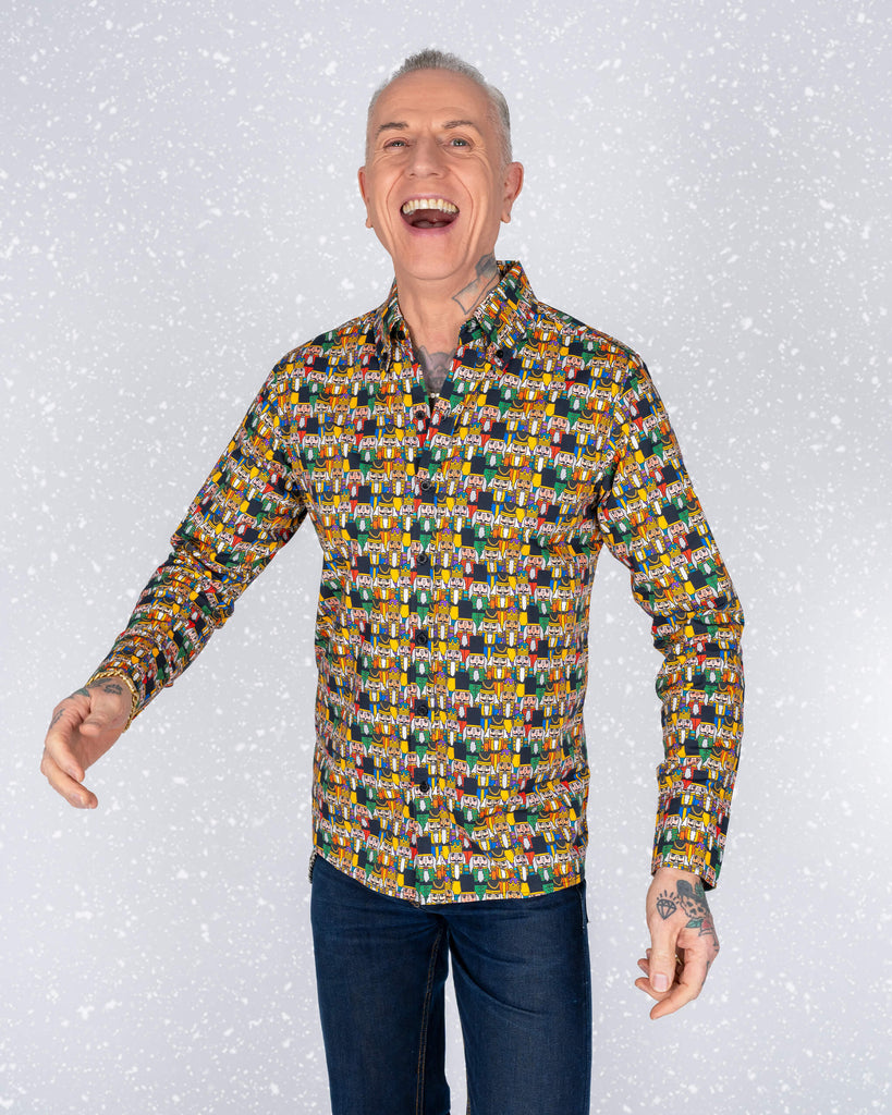 James stands confidently in a Nutcracker print shirt with a snowy background. His tattoos and bright smile complement the quirky and bold design of the shirt.