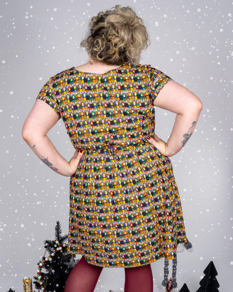 Back view of Maddie in the Nutcracker print dress, showing the dress’s shape and print consistency, set against a festive backdrop with snow effects and Christmas-themed props.