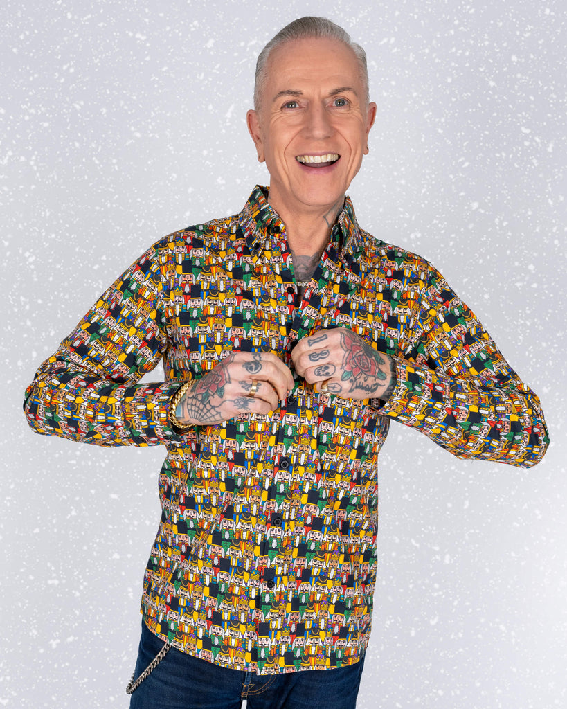 James stands confidently in a Nutcracker print shirt with a snowy background. His tattoos and bright smile complement the quirky and bold design of the shirt.