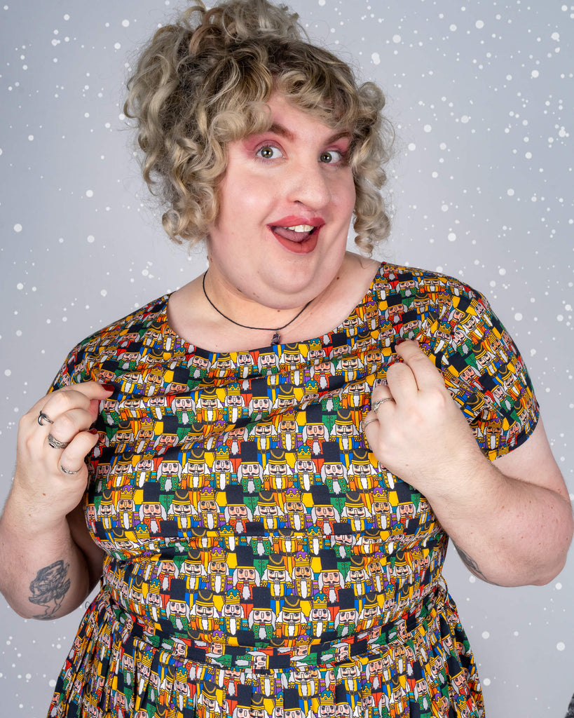 Close-up of Maddie pointing to the Nutcracker print, showing off the dress’s fun and festive design by Waffle Mama. The snowy background adds to the seasonal theme.