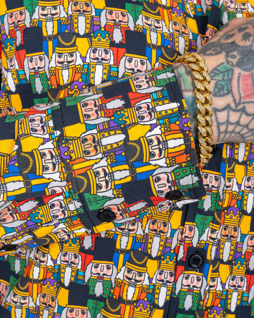 Close-up of the Nutcracker print on a long-sleeve button-up shirt, showcasing intricate details of the Nutcracker characters in a vibrant palette of red, green, blue, and yellow. The sleeve cuff features the same pattern, with black buttons.
