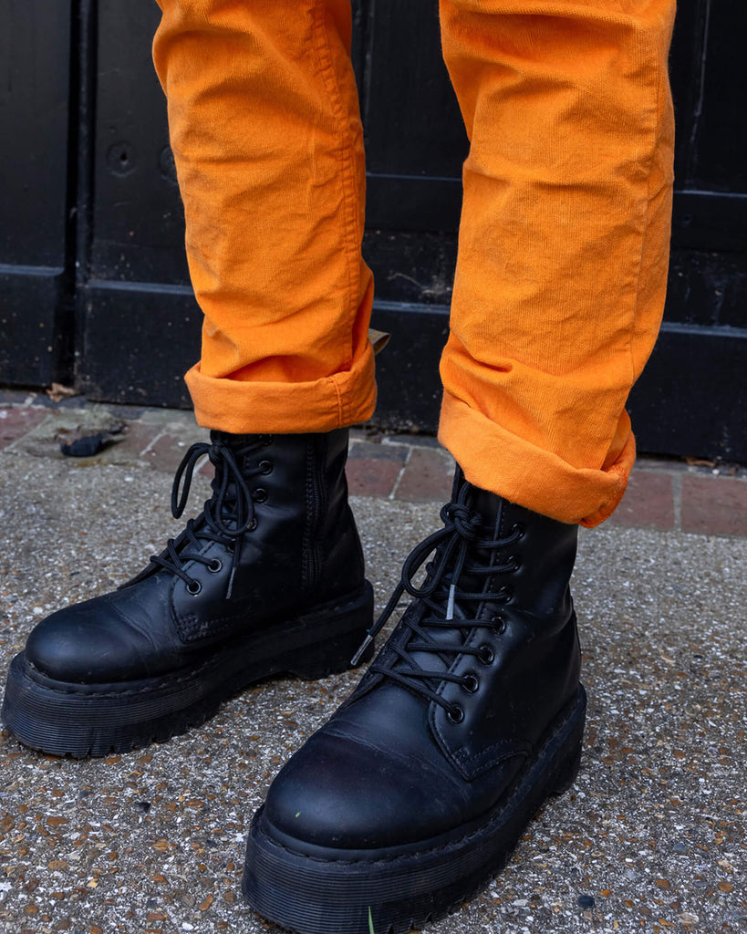 Close up of models legs wearing Highlighter Orange Stretch Corduroy Dungarees paired with chunky black boots. The bottoms of the legs are turned up to reveal the model's boots.
