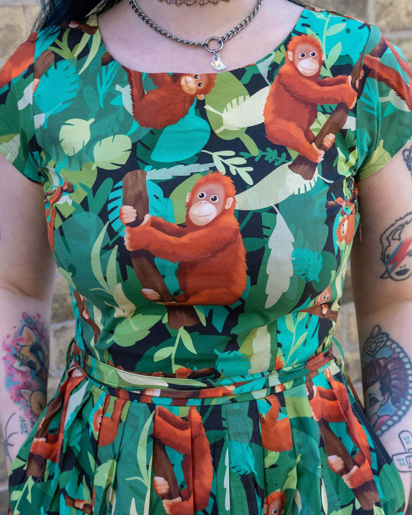 Close up of Faeryn is stood outside in Hove in a mews wearing Orangutan Stretch Belted Tea Dress with Pockets. The green dress has an all over orangutan print with leaves and branches.