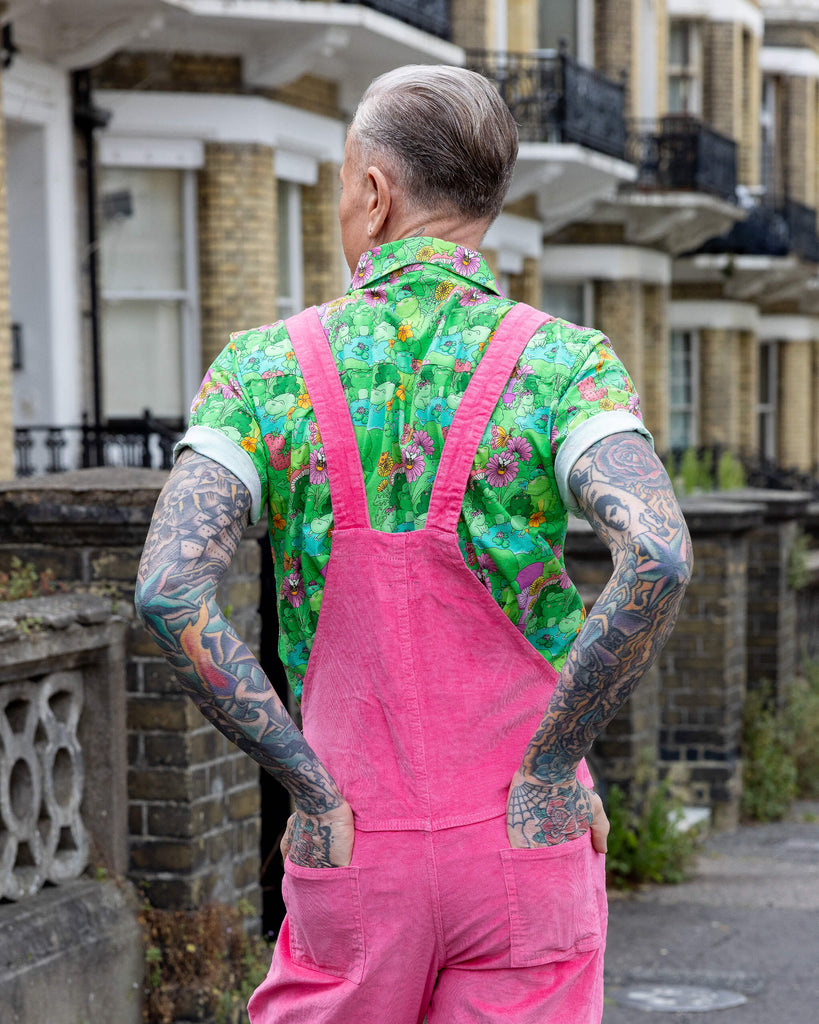 James is wearing Pink Stretch Corduroy Dungarees, paired with the Mushroom Babes frogs green short sleeve shirt and black and white trainers. The dungarees are a bright pink all over colour with Run & Fly logo on the front bib. He is stood with his back to the camera and hands in the back pockets of the dungarees 